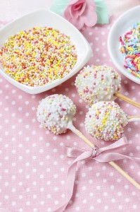White cake pops on pink dotted table cloth. Colorful sprinkles